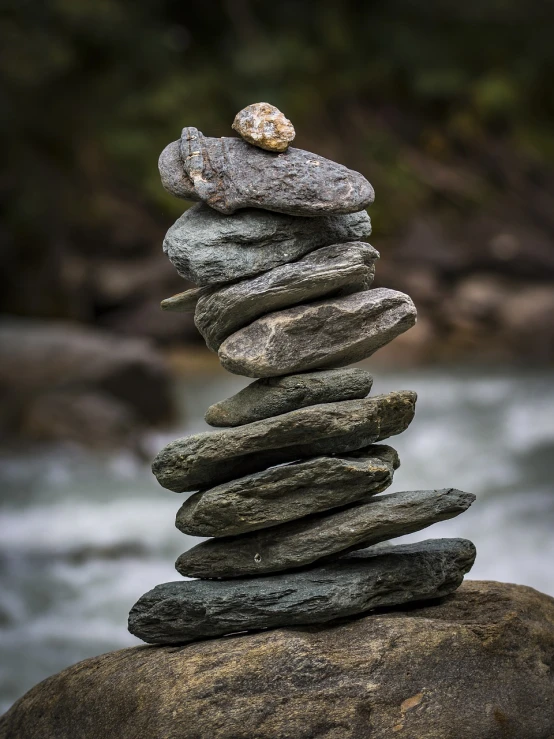 a pile of rocks sitting on top of a rock next to a river, a statue, by Aleksander Gierymski, shutterstock, naturalism, balancing the equation, vertical orientation, stepping on towers, texture