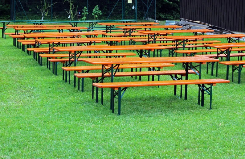 a group of wooden benches sitting on top of a lush green field, by Hans Schwarz, octoberfest, orange and white color scheme, rows of canteen in background, very accurate photo