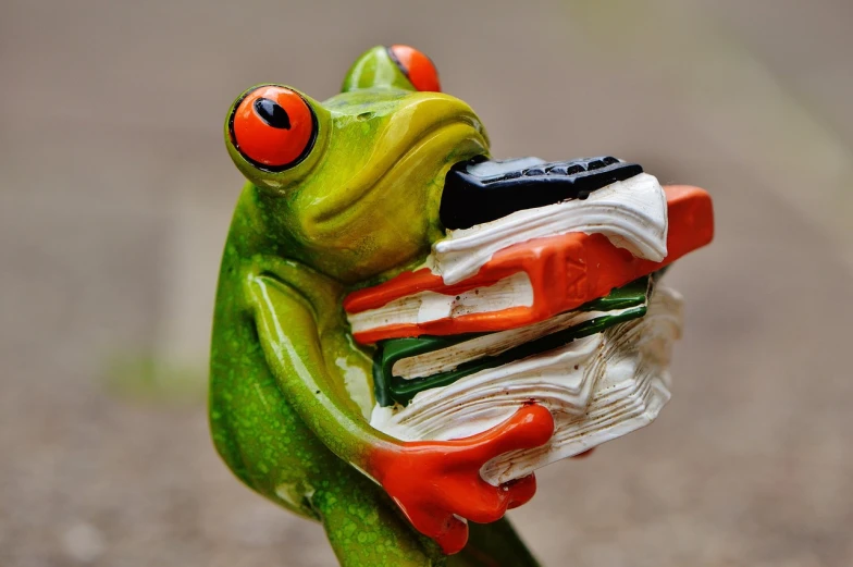 a figurine of a frog holding a stack of books, by Robert Brackman, flickr, eating, up close picture, far away from camera, a brightly coloured