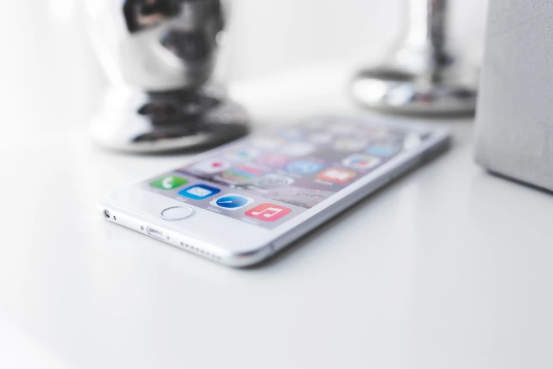 a cell phone sitting on top of a white table, a picture, by Julian Allen, pexels, apple design, blurred detail, glossy white metal, shot on iphone 6