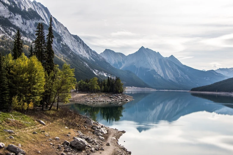 a body of water surrounded by trees and mountains, by Raymond Normand, shutterstock, rocky lake shore, clean environment, erosion, great sense of depth