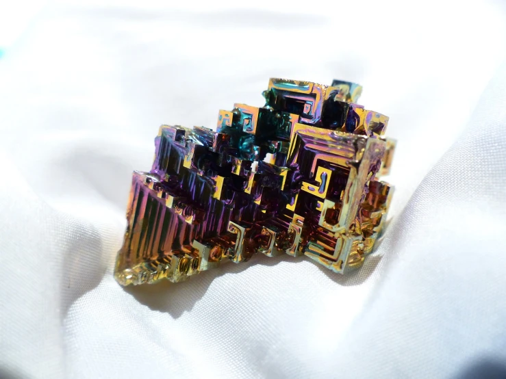 a close up of a metal object on a white cloth, a macro photograph, unsplash, crystal cubism, vibrant bismuth material, jewelry iridescent, side view intricate details, solarised