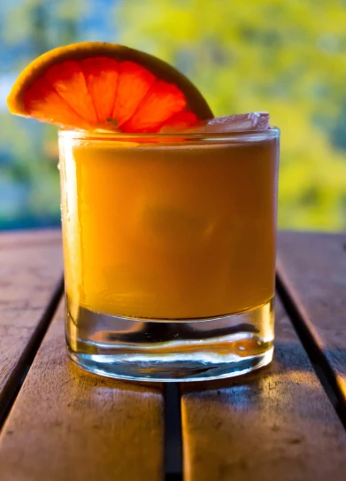 a drink sitting on top of a wooden table, by Jan Rustem, sliced grapefruit, vivid colors!, short dof, drinks bourbon