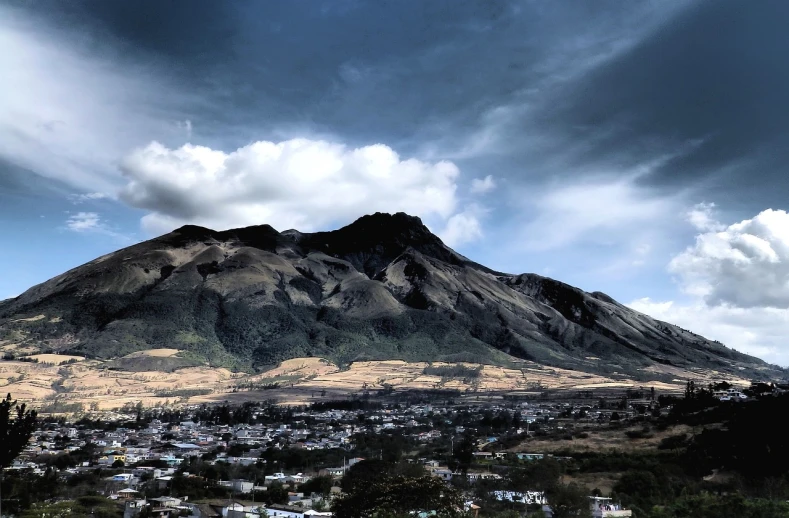 a mountain with a town below it under a cloudy sky, unsplash, quito school, professional iphone photo, a dark, blonde, an ancient