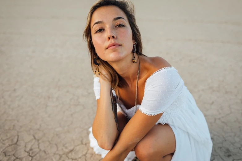 a woman sitting on the ground in a white dress, a portrait, inspired by Zoë Mozert, unsplash, beautiful tan mexican woman, standing in desert, close up portrait photo, dua lipa