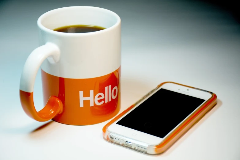 a cup of coffee next to a cell phone, by Niko Henrichon, flickr, happening, orange and white, hello, saying, covered in