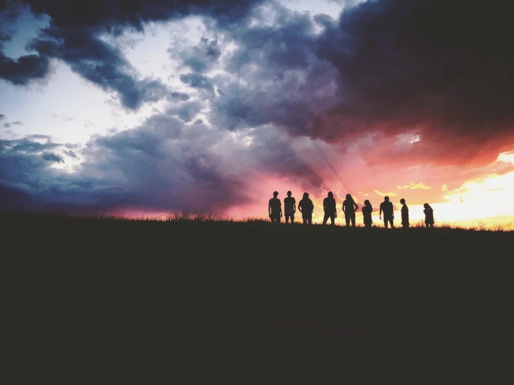 a group of people standing on top of a grass covered field, a picture, pexels, romanticism, moody sunset and dramatic sky, us soldiers, iphone photo, in a row