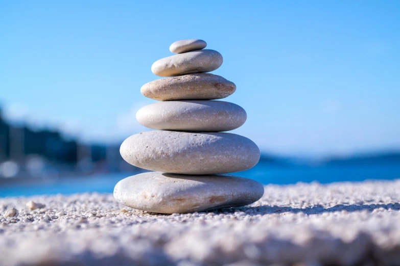 a stack of rocks sitting on top of a sandy beach, a picture, pexels, minimalism, relaxed. blue background, balancing the equation, mobile wallpaper, bright white castle stones