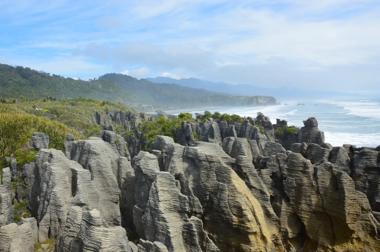 a group of rocks sitting on top of a lush green hillside, a matte painting, abel tasman, black domes and spires, soft-sanded coastlines, shiny layered geological strata