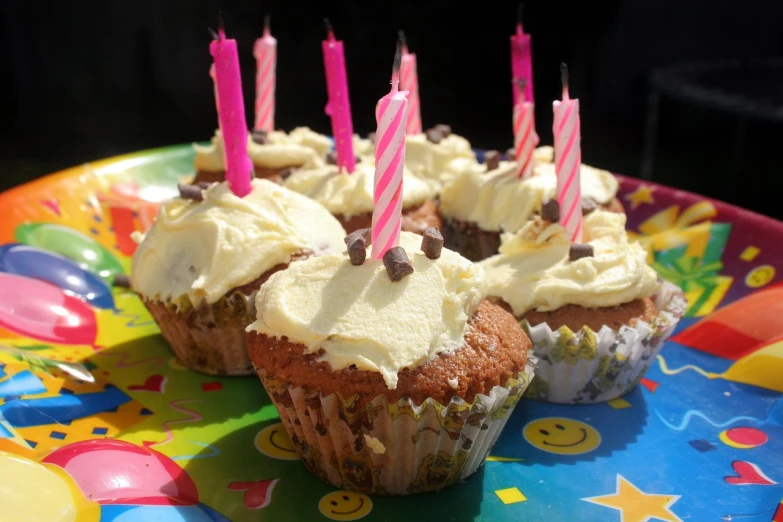 a plate topped with cupcakes covered in frosting and lit candles, a photo, by Helen Berman, pixabay, on flickr in 2 0 0 3, aged 4 0, white with chocolate brown spots, at a birthday party