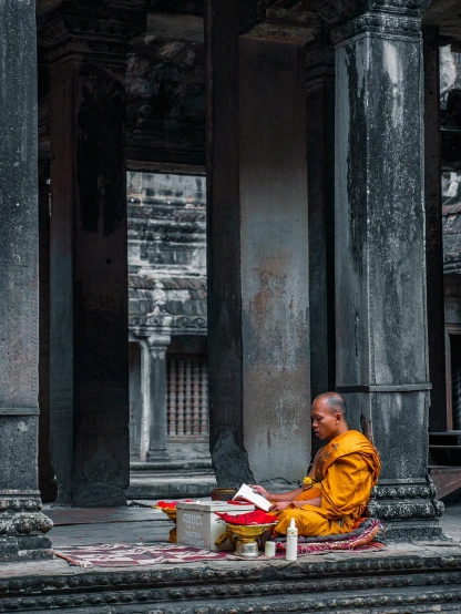 a monk sitting on the ground reading a book, pexels contest winner, minimalism, angkor wat, cyberpunk temple, adorned pillars, man holding spear