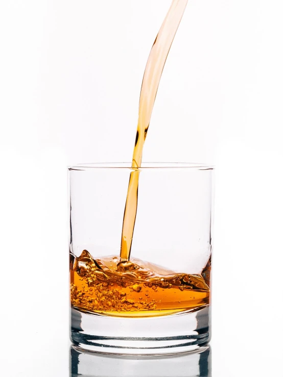 a glass filled with liquid sitting on top of a table, by Jan Rustem, pexels, dau-al-set, set against a white background, drinking whiskey, pouring, detailed product photo