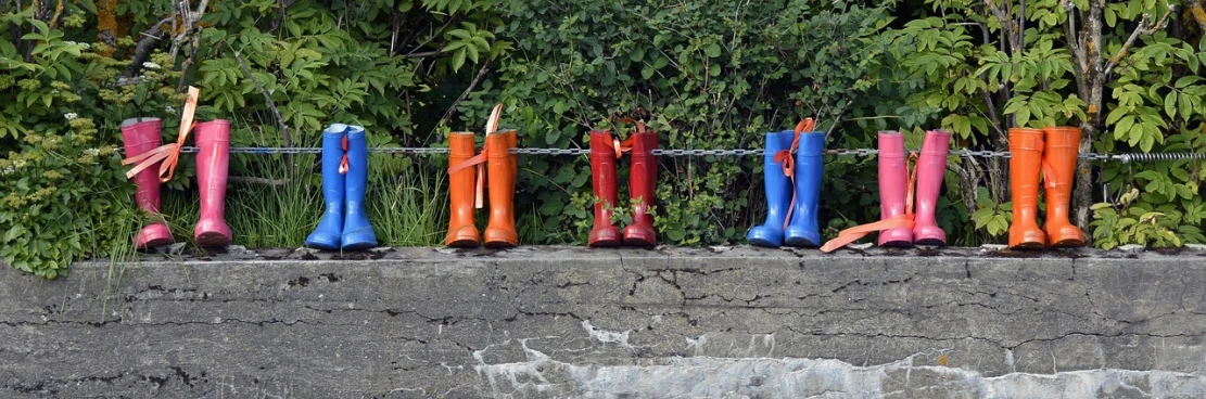 a row of colorful rain boots sitting on top of a cement wall, pixabay, red orange blue beige, on the coast, hoofs, bridge