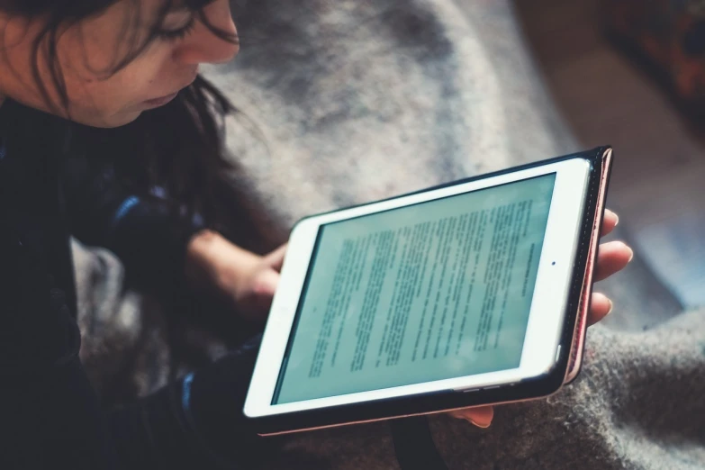 a woman sitting on a couch holding a tablet computer, by Adam Marczyński, pexels, book library studying, bokeh”, bottom angle, grungy