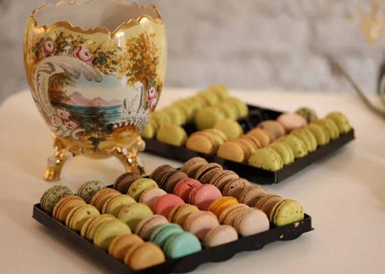 a couple of trays of macarons on a table, by Zsuzsa Máthé, rococo, various colors, award-winning masterpiece, pot, made of glazed