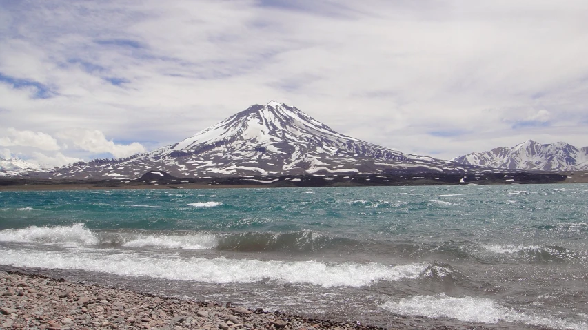 a body of water with a mountain in the background, a picture, by Andrei Kolkoutine, flickr, volcano, with snow on its peak, windy beach, may)