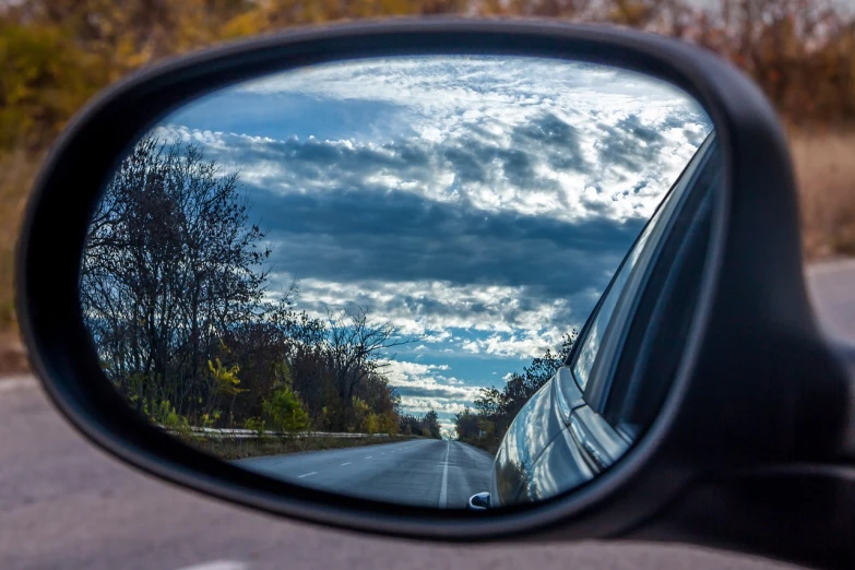 a rear view mirror of a car on the side of the road, by Tom Carapic, realistic wide angle photo, partly cloudy day, autum, reportage photo