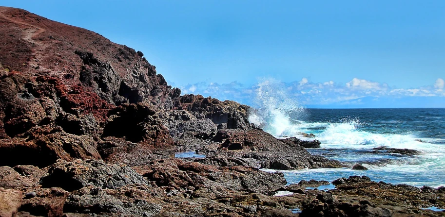 a man riding a surfboard on top of a rocky beach, a photo, by Jim Nelson, happening, panorama, the earth sprouts lava, ((rocks)), spikey rocks