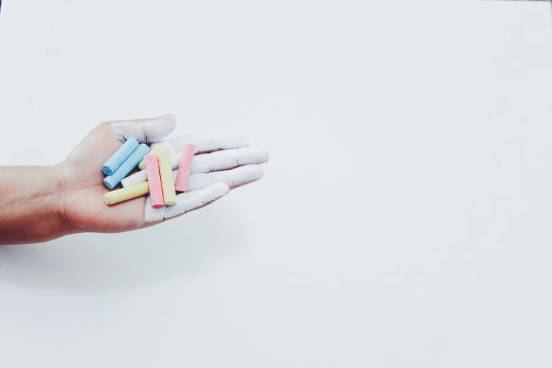 a person holding a bunch of chalks in their hand, by Emma Andijewska, visual art, white colors, minimal art style, colorful plastic, hand - tinted