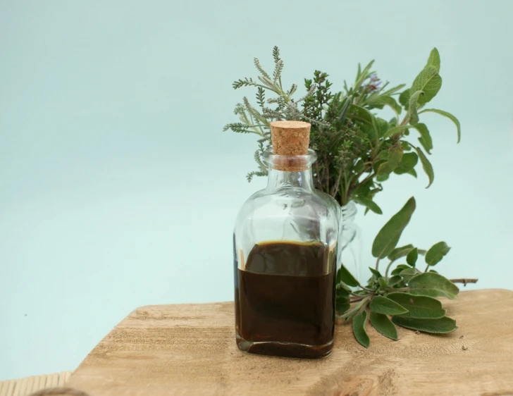 a bottle filled with liquid sitting on top of a wooden table, inspired by Ceferí Olivé, unsplash, renaissance, herbs, black oil bath, plants in glass vase, brown sauce