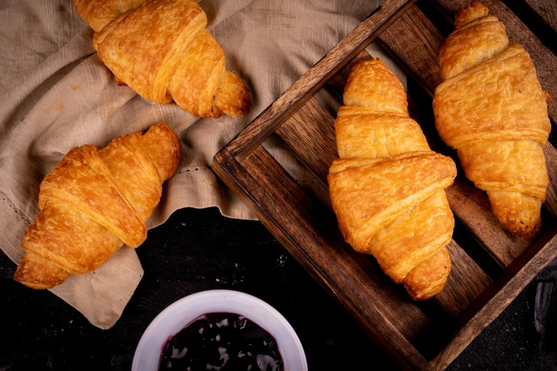 a couple of croissants sitting on top of a wooden tray, a portrait, inspired by Géza Dósa, shutterstock, 🎀 🗡 🍓 🧚, dark vignette, oklahoma, stock photo