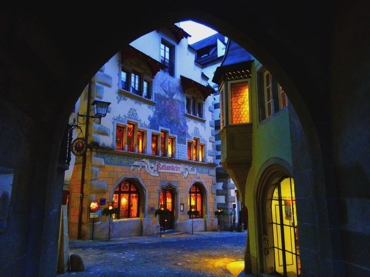 a person walking down a cobblestone street at night, a photo, by Karl Hofer, flickr, art nouveau, in a medieval tavern at night, swiss architecture, an archway, movie set”