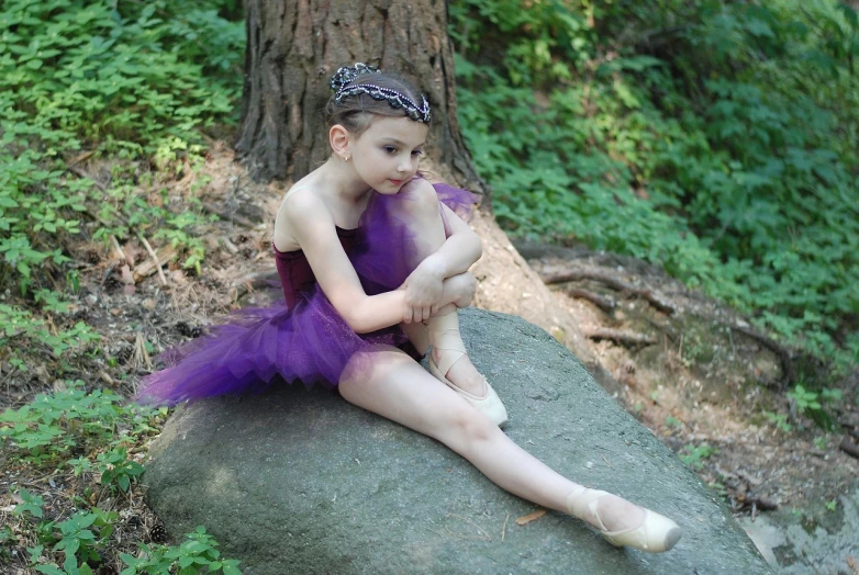 a little girl in a purple tutu sitting on a rock, inspired by Elizabeth Polunin, flickr, with a few scars on the tree, ballet performance photography, fey queen of the summer forest, file photo