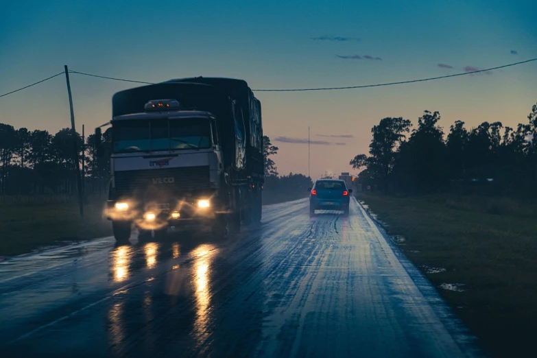 a truck driving down a wet road next to a car, a picture, unsplash, realism, humid evening, brazilian, ad image