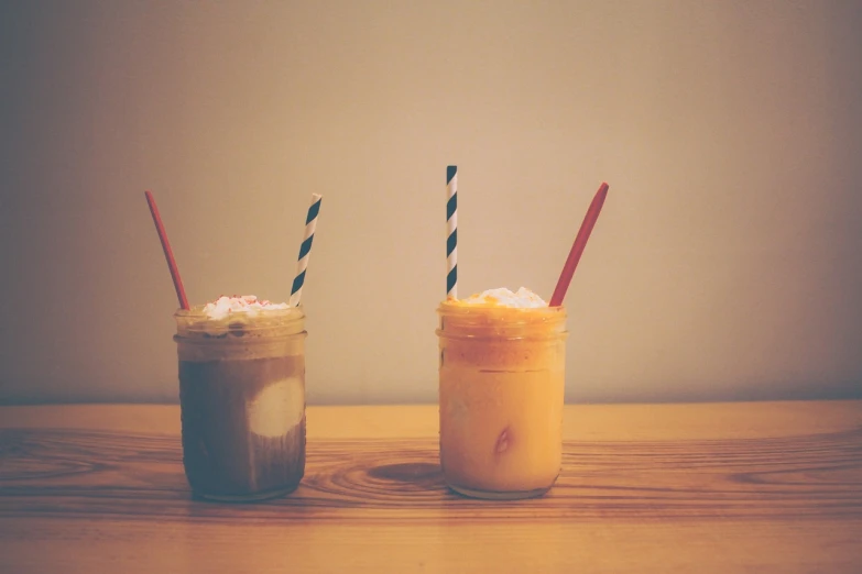 a couple of drinks sitting on top of a wooden table, pexels, minimalism, milkshake, jars, brown and cream color scheme, slush))