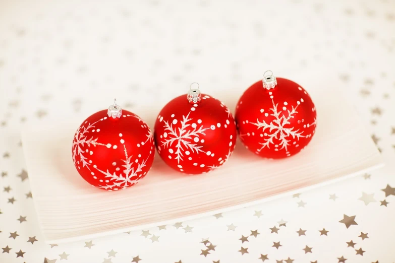 three red christmas ornaments sitting on top of a white plate, miniature product photo, white stars in the background, highly detailed product photo, spheres