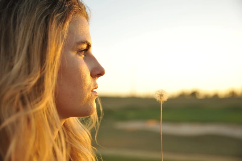 a woman with long blonde hair blowing a dandelion, a portrait, by Dan Luvisi, unsplash, precisionism, looking off into the sunset, 60mm portrait, looking out at a sunset, stubble