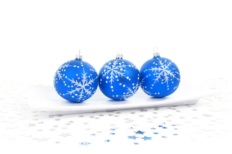 three blue christmas ornaments sitting on top of a white plate, a photo, document photo, high quality product photo, white stars in the background, with a white background