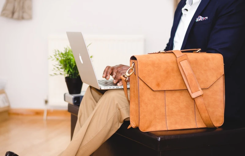 a man sitting in a chair with a briefcase and a laptop, a picture, by Romain brook, pexels, brown clothes, details and vivid colors, bag, wearing business casual dress