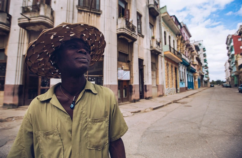 a man wearing a straw hat standing in the middle of a street, cuban setting, dark skinned, shot from a low angle, 💣 💥