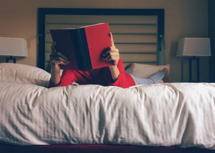 a person laying on a bed reading a book, a stock photo, by Carey Morris, wearing red clothes, hotel room, diy, compressed jpeg