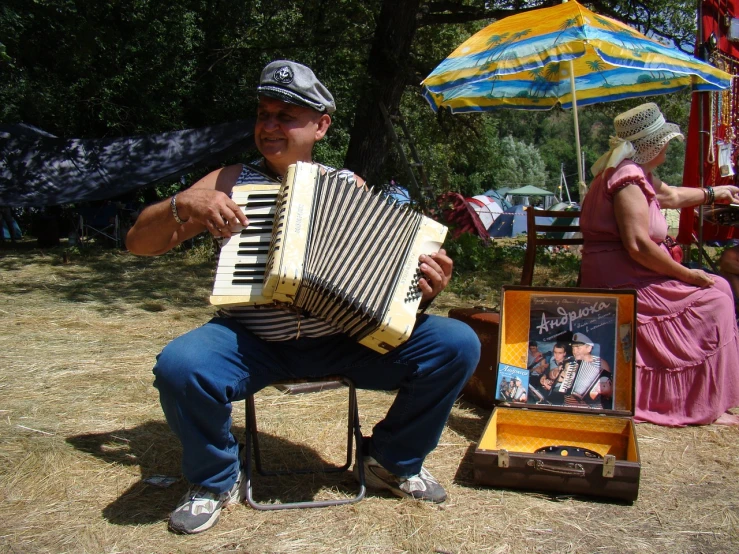 a man sitting on a chair playing an accordion, a photo, by Eugeniusz Zak, flickr, picnic, vinyl, traditional corsican, where a large