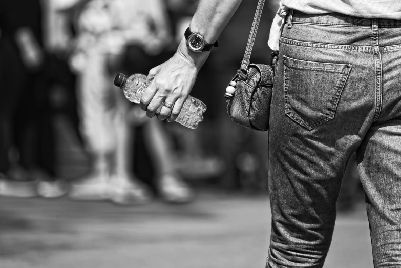 a black and white photo of a person holding a bottle of water, by Mirko Rački, pexels, happening, bag over the waist, street wear, uhd candid photo of dirty, ( ( ( wearing jeans ) ) )