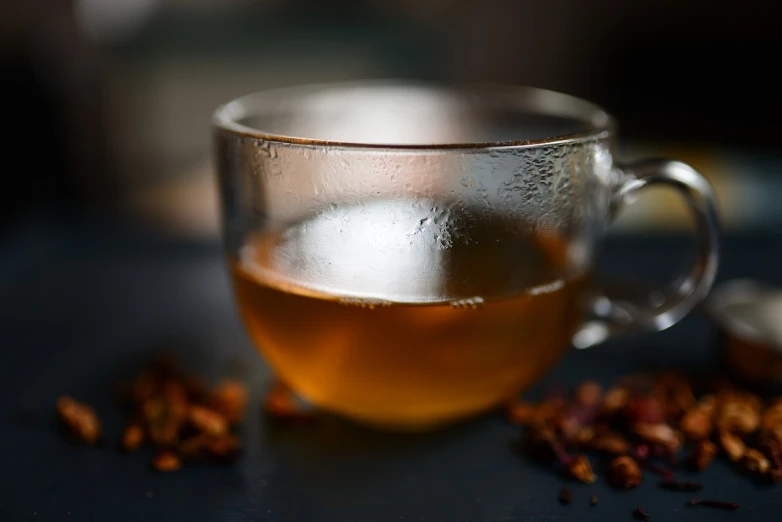 a close up of a cup of tea on a table, by Frederik Vermehren, pexels, renaissance, against dark background, rum, sichuan, herbs