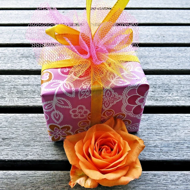 a small gift box sitting on top of a wooden table, by Alice Mason, pixabay contest winner, pink and orange, pink rose, celebrating a birthday, istockphoto