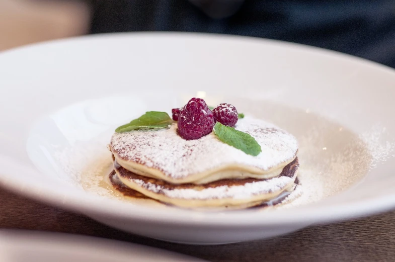 a white plate topped with pancakes covered in powdered sugar and raspberries, romanticism, ivy's, manuka, jaquet droz, ripple