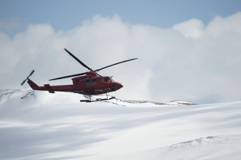 a red helicopter flying over a snow covered mountain, a photo, by Edwin Georgi, shutterstock, hurufiyya, helipad, left profile, high res photo, skidding