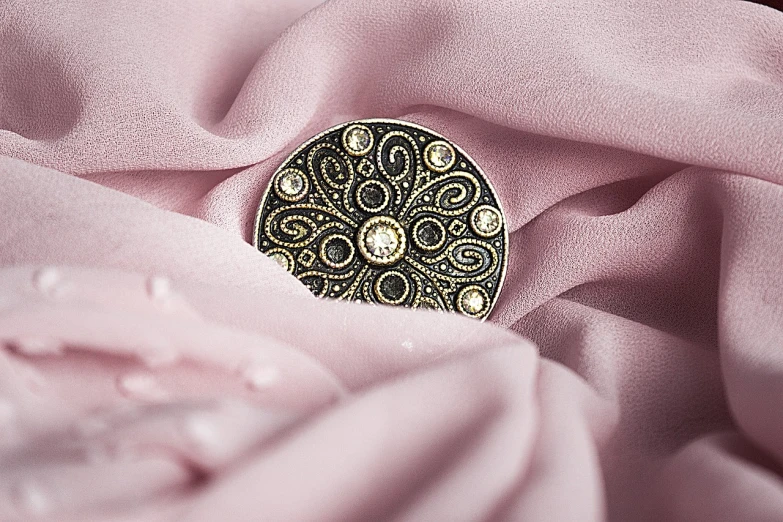 a brooch sitting on top of a pink cloth, flickr, baroque, ring flash closeup photograph, close-up product photo, in clothes! intricate, dolman