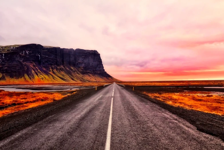 an empty road with a mountain in the background, by Hallsteinn Sigurðsson, pexels contest winner, realism, pink landscape, cliffs, 4k vertical wallpaper, colorful sunset