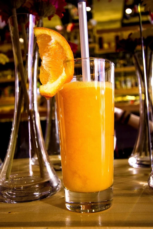 a glass of orange juice sitting on top of a wooden table, by Juan Giménez, renaissance, bar, high quality product image”, sao paulo, excitement