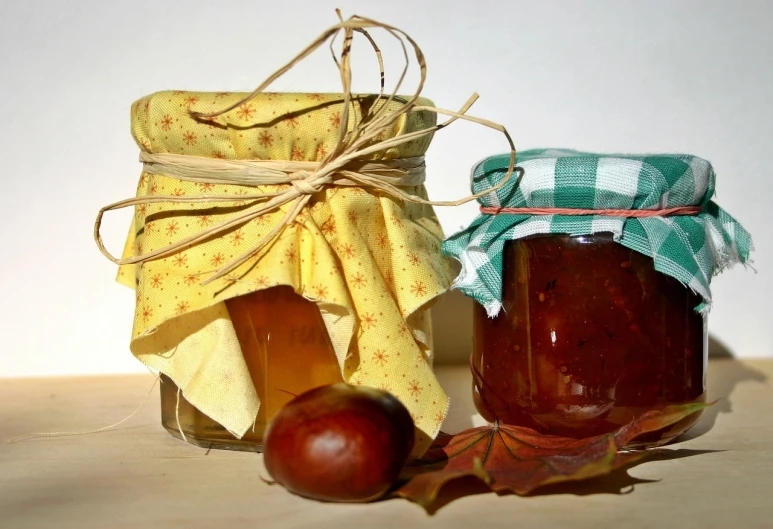 a couple of jars of food sitting on top of a table, by Aleksander Gierymski, pixabay, leaves and simple cloth, marmalade, 1 6 x 1 6, wax