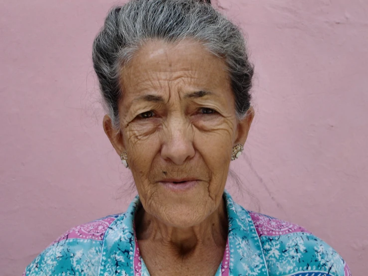 a woman standing in front of a pink wall, a portrait, by Ramón Silva, flickr, the look of an elderly person, large eyebrows, 30-year-old woman from cuba, face center close-up