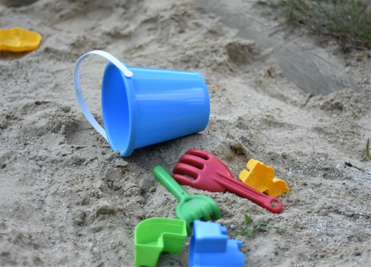 a blue bucket sitting on top of a sandy beach, a picture, pexels, plasticien, toys, hand made, green blue red colors, high - quality