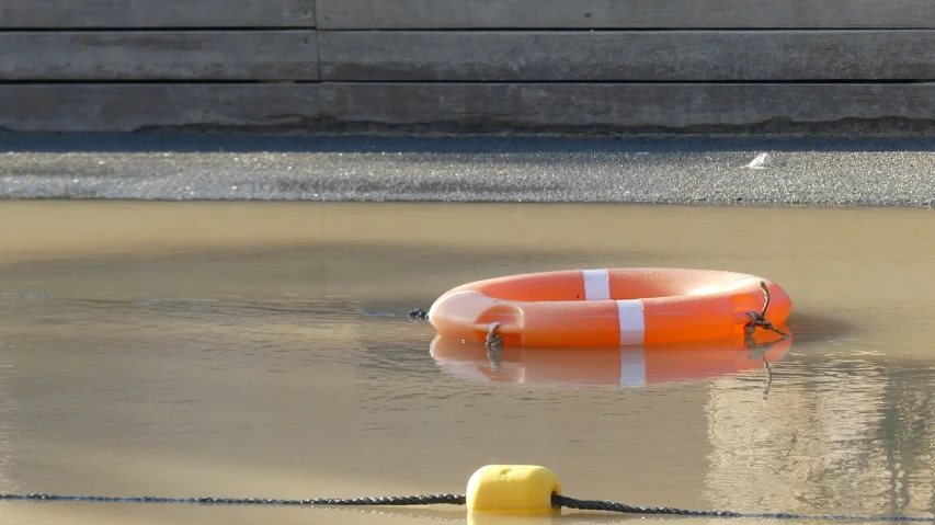 a life preserver floating in a puddle of water, a photo, by Richard Carline, shutterstock, plasticien, helipad, harbor, round-cropped, an orange