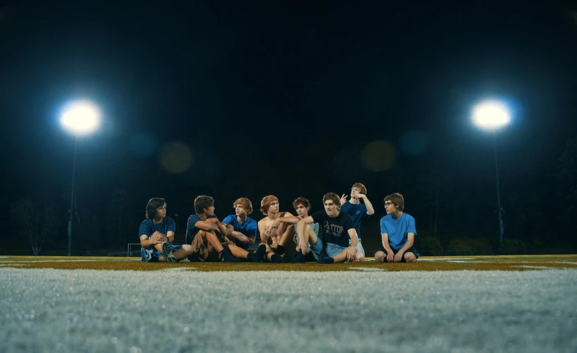 a group of people sitting on top of a soccer field, by Elsa Bleda, unsplash, conceptual art, still from stranger things, blue hour stars, cute boys, camp x-ray