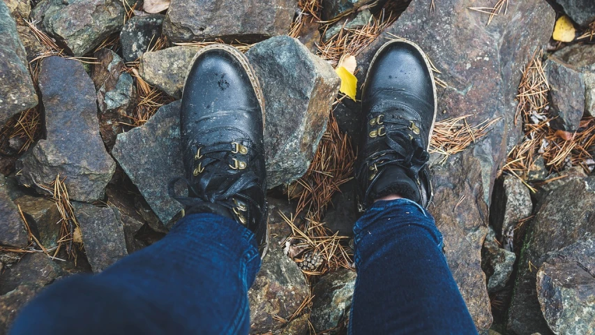 a person standing on top of a pile of rocks, black leather boots, instagram photo, charcoal and yellow leather, tight blue jeans and cool shoes